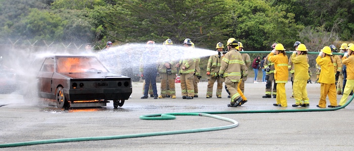 Girls Firefighter Camp Attendees Putting Out Fire on Car with Hose