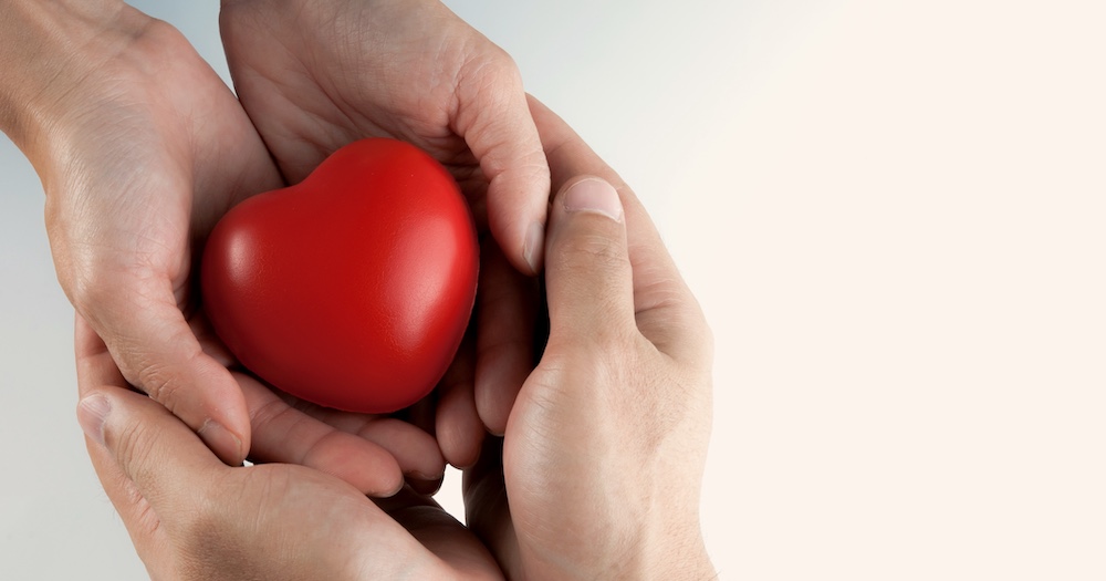 Two people holding hands on top of eachother cupping heart